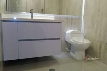 Un mueble de lavamanos a medida, fabricado con tableros RH resistentes a la humedad en acabado madera clara, con mesón de cuarzo blanco y lavamanos de incrustar. Se aprecia la altura ergonómica instalada para la comodidad diaria en al Remodelacion de baños Bogotá