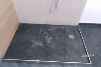Ducha a ras de suelo con regadera de techo, regadera de mano, nicho empotrado y revestimiento en madera en remodelación de baño accesible en Bogotá  por Francisco Cruz Interiores