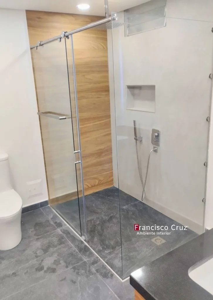 Ducha con división de vidrio templado, muro de acento tipo madera, piso oscuro y nicho de almacenamiento.