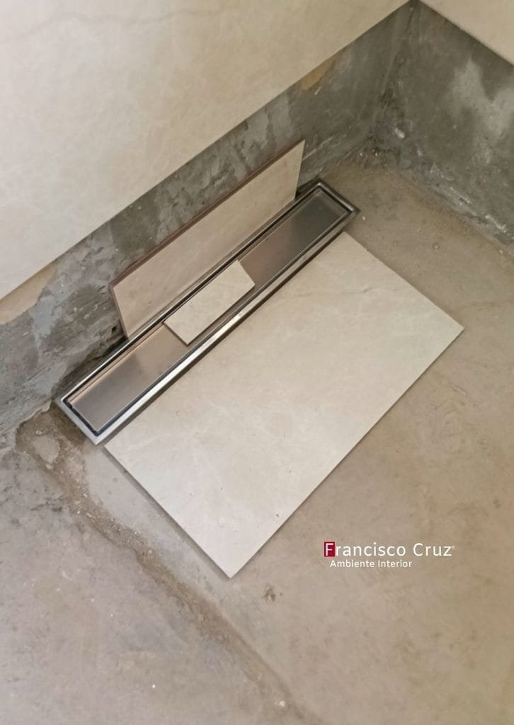 Desagüe lineal de acero inoxidable presentado sobre el piso junto a una pieza de cerámica.