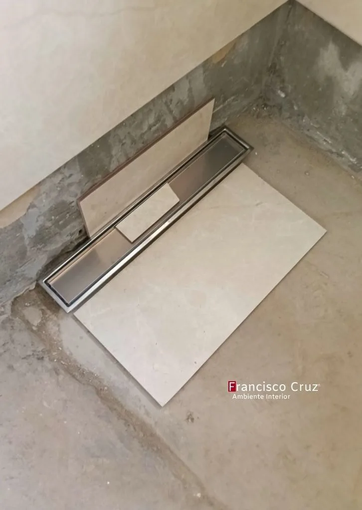 Desagüe lineal de acero inoxidable presentado sobre el piso junto a una pieza de cerámica.