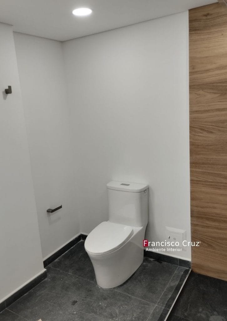 Sanitario contemporáneo con espacio lateral libre, piso en porcelanato oscuro y revestimiento en madera en baño accesible remodelado en Bogotá Francisco Cruz Interiores