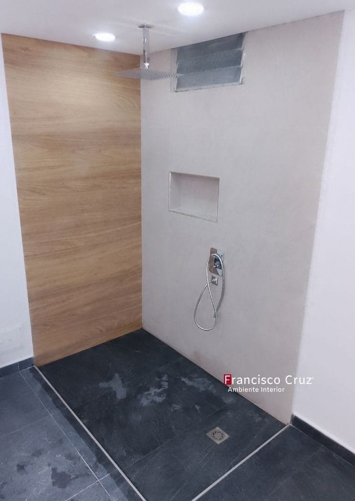 Ducha a ras de suelo con regadera de techo, regadera de mano, nicho empotrado y revestimiento en madera en remodelación de baño accesible en Bogotá  Francisco Cruz Interiores