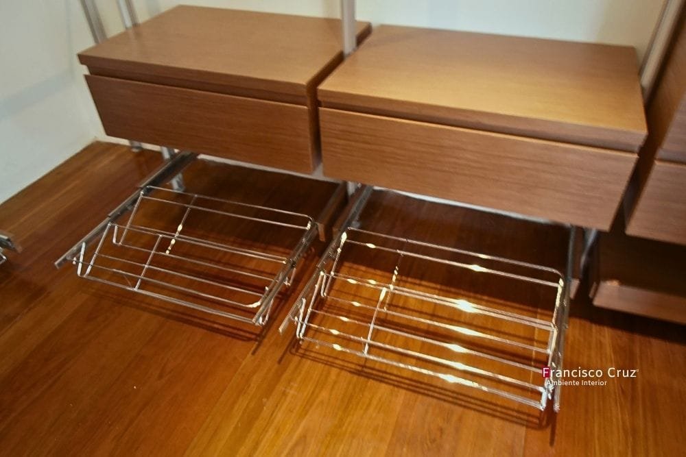 Zapateras extraíbles de rejilla metálica bajo cajones de madera en un walk in closet a medida